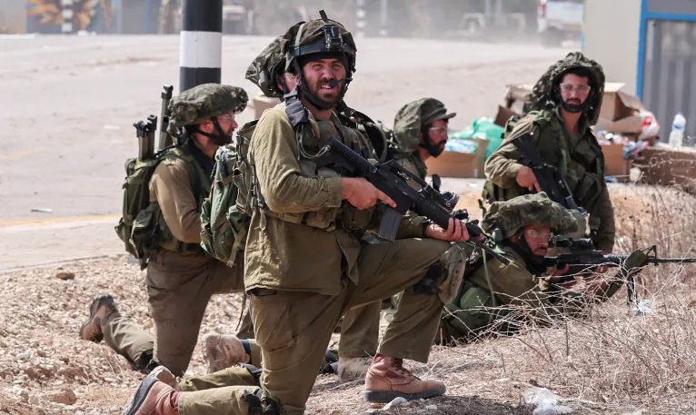Israeli soldiers take position next to a road in Kfar Aza, south of Israel bordering the Gaza Strip, on October 10, 2023 [Thomas Coex/AFP]